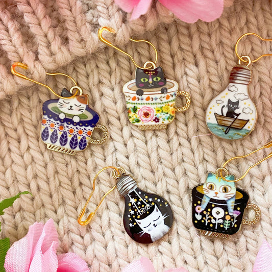 Cat in Teacup Stitch Markers Set – Whimsical stitch markers with adorable cats in teacups and lightbulbs for knitting and crochet.